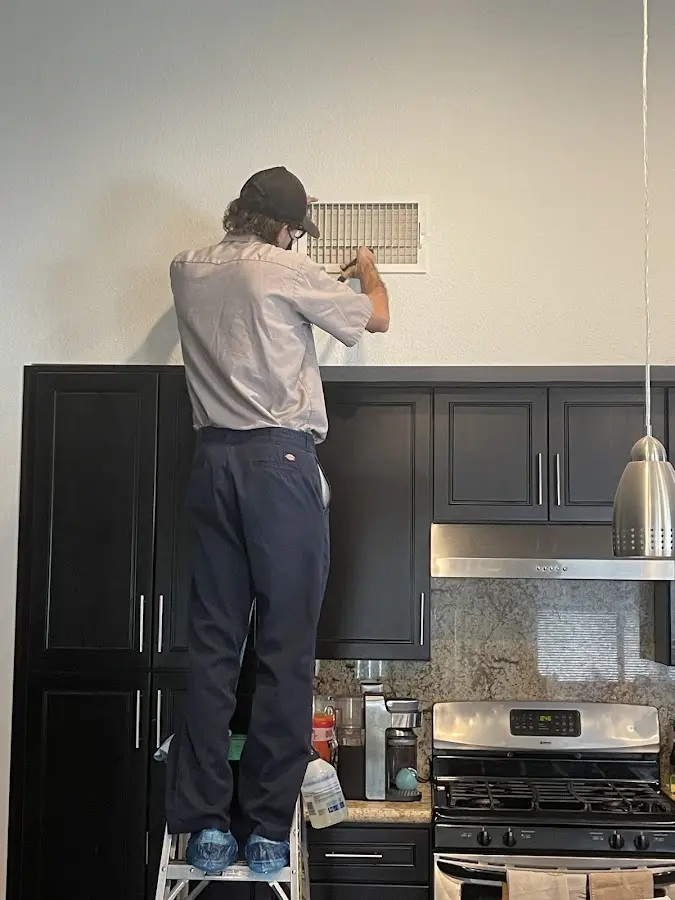 Technician inspecting an air vent during HVAC service in Iowa Colony